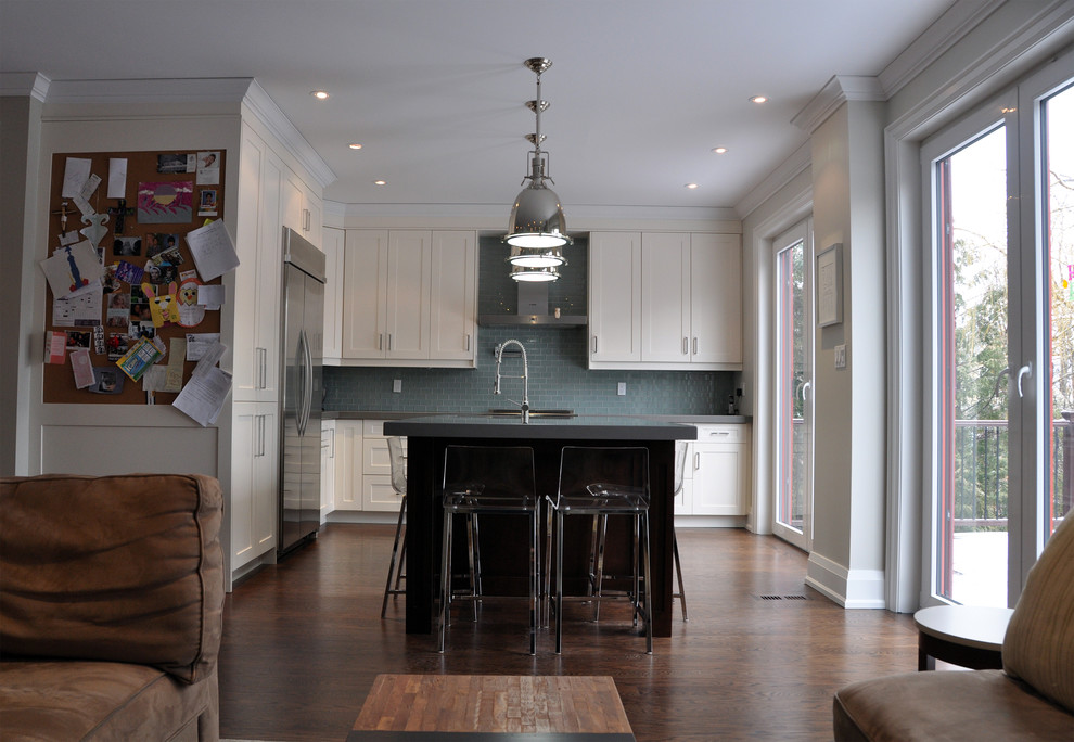 Example of a mid-sized trendy l-shaped medium tone wood floor open concept kitchen design in Toronto with an undermount sink, shaker cabinets, white cabinets, solid surface countertops, gray backsplash, glass tile backsplash, stainless steel appliances and an island