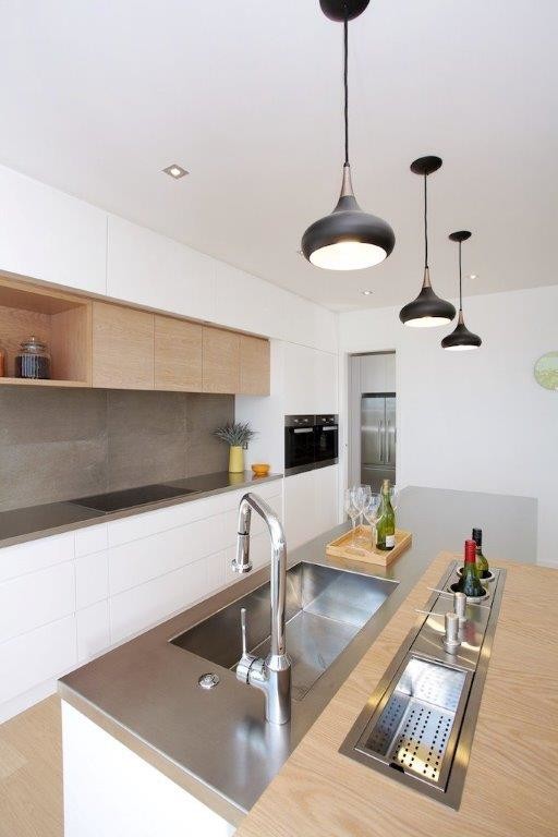 Exempel på ett mellanstort modernt kök, med en integrerad diskho, luckor med infälld panel, vita skåp, bänkskiva i rostfritt stål, brunt stänkskydd, stänkskydd i keramik, svarta vitvaror, ljust trägolv, flera köksöar och brunt golv