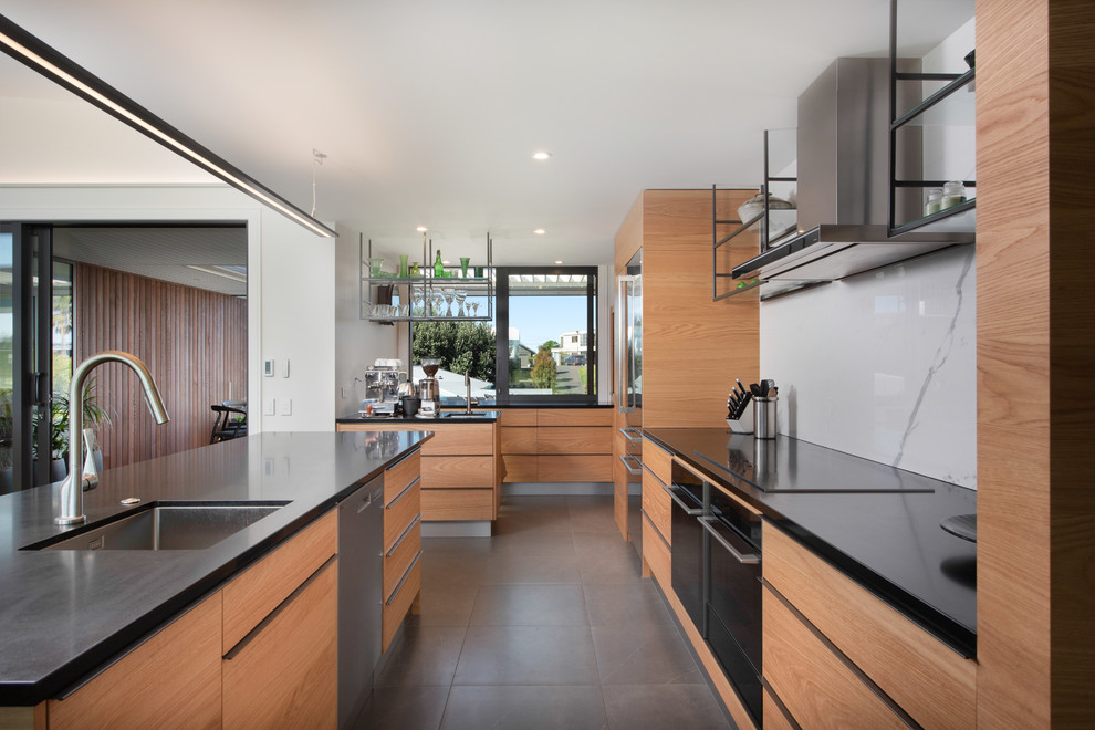 Foto di un cucina con isola centrale contemporaneo con lavello sottopiano, ante lisce, ante in legno chiaro, paraspruzzi bianco, elettrodomestici neri, pavimento grigio e top nero
