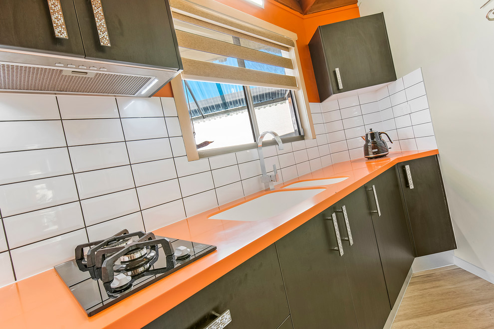 Modelo de cocina lineal moderna pequeña cerrada con fregadero integrado, encimera de acrílico, salpicadero amarillo, salpicadero de azulejos tipo metro y encimeras naranjas