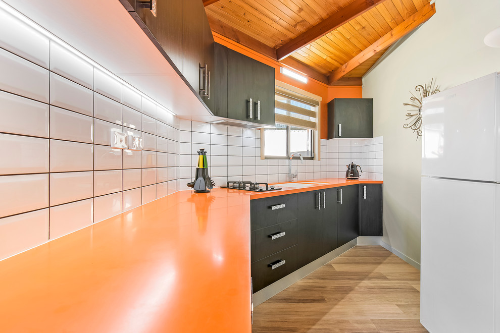 На фото: маленькая отдельная, прямая кухня в стиле модернизм с монолитной мойкой, столешницей из акрилового камня, желтым фартуком, фартуком из плитки кабанчик и оранжевой столешницей для на участке и в саду