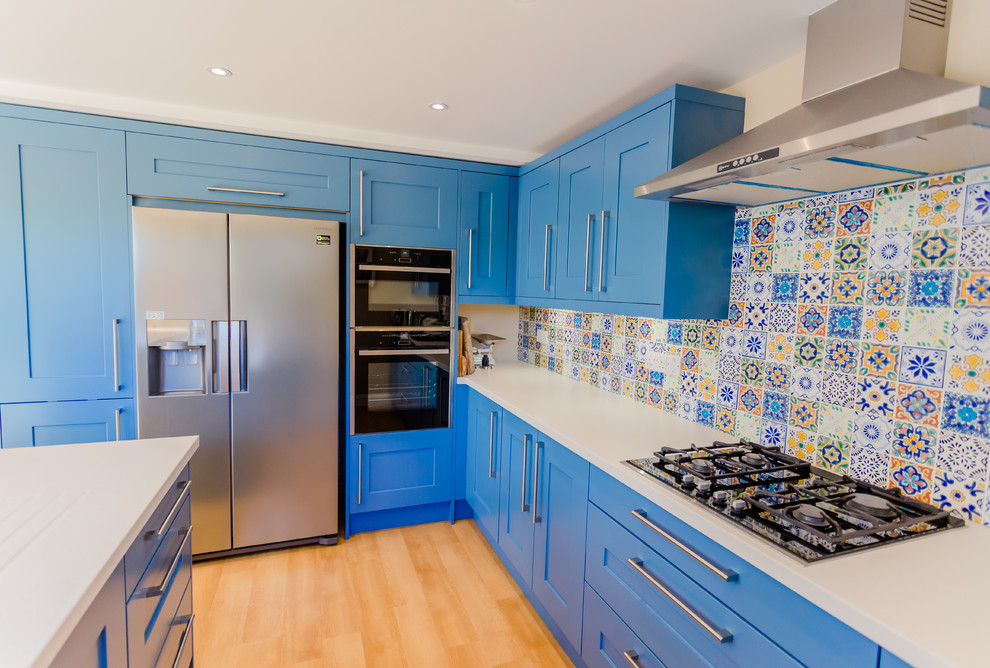 Idéer för ett mellanstort modernt kök, med en undermonterad diskho, skåp i shakerstil, blå skåp, bänkskiva i kvarts, blått stänkskydd, stänkskydd i mosaik, rostfria vitvaror, laminatgolv, en halv köksö och beiget golv