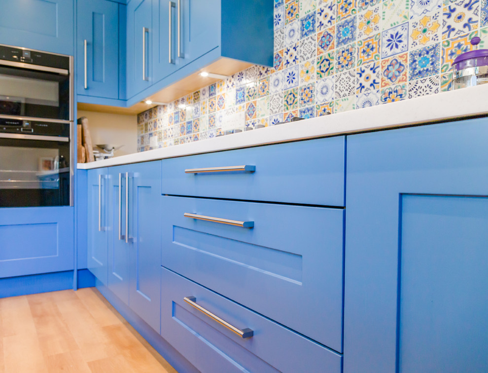 ロンドンにあるお手頃価格の中くらいなコンテンポラリースタイルのおしゃれなキッチン (アンダーカウンターシンク、シェーカースタイル扉のキャビネット、青いキャビネット、クオーツストーンカウンター、青いキッチンパネル、モザイクタイルのキッチンパネル、シルバーの調理設備、ラミネートの床、ベージュの床) の写真