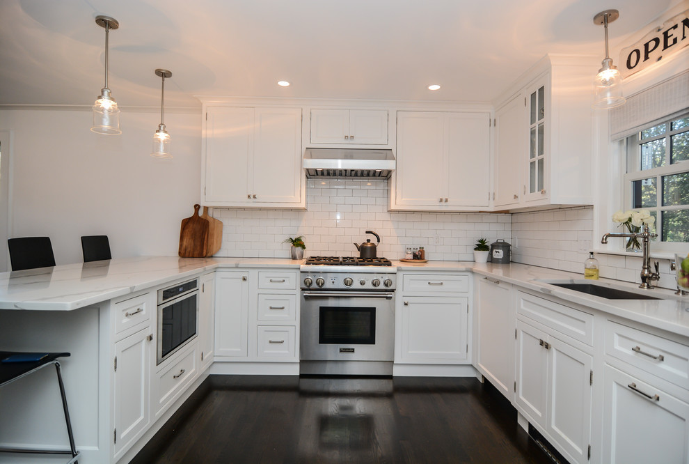 Modern inredning av ett mellanstort kök, med en enkel diskho, skåp i shakerstil, vita skåp, marmorbänkskiva, vitt stänkskydd, stänkskydd i tunnelbanekakel, rostfria vitvaror, mörkt trägolv, en halv köksö och svart golv