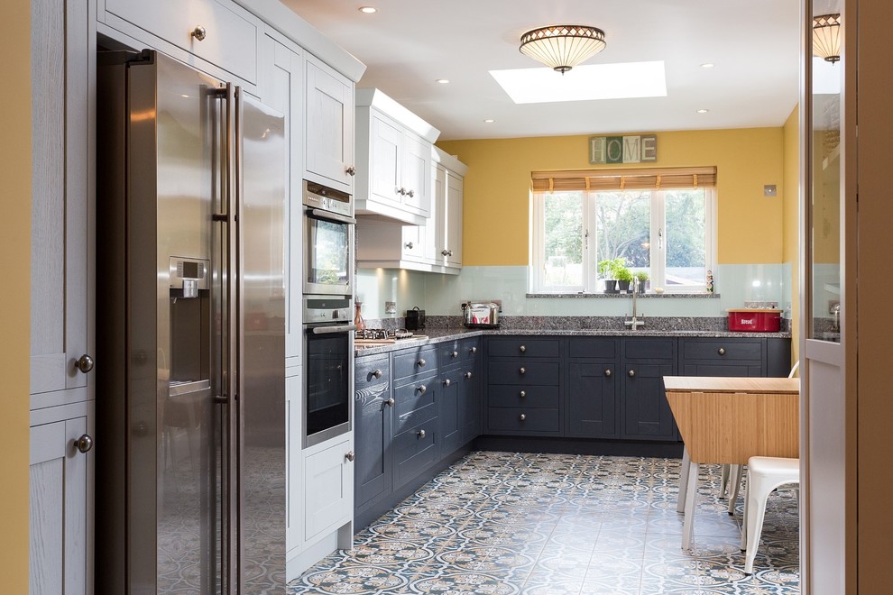 This is an example of a medium sized traditional l-shaped kitchen/diner in London with shaker cabinets, grey cabinets, granite worktops, green splashback, glass sheet splashback, porcelain flooring, no island and multi-coloured floors.