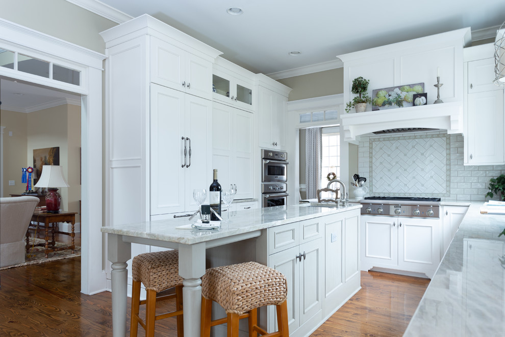 Example of a large classic u-shaped brown floor and dark wood floor eat-in kitchen design in Atlanta with white cabinets, quartzite countertops, an island, recessed-panel cabinets, white backsplash, an undermount sink, subway tile backsplash, paneled appliances and beige countertops