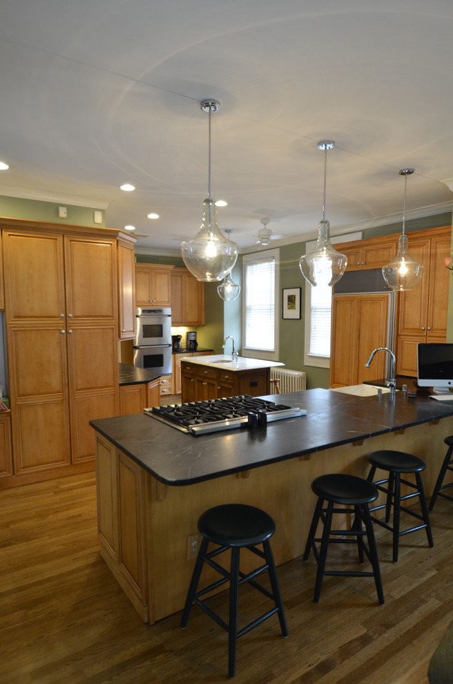 Exemple d'une cuisine chic en bois brun avec un évier de ferme, un placard à porte affleurante, un plan de travail en stéatite, un électroménager en acier inoxydable, un sol en bois brun et îlot.