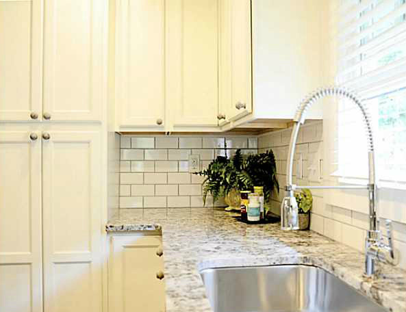 Moderne Küche in L-Form mit weißen Schränken, Küchenrückwand in Weiß, Rückwand aus Metrofliesen und Küchengeräten aus Edelstahl in Charlotte