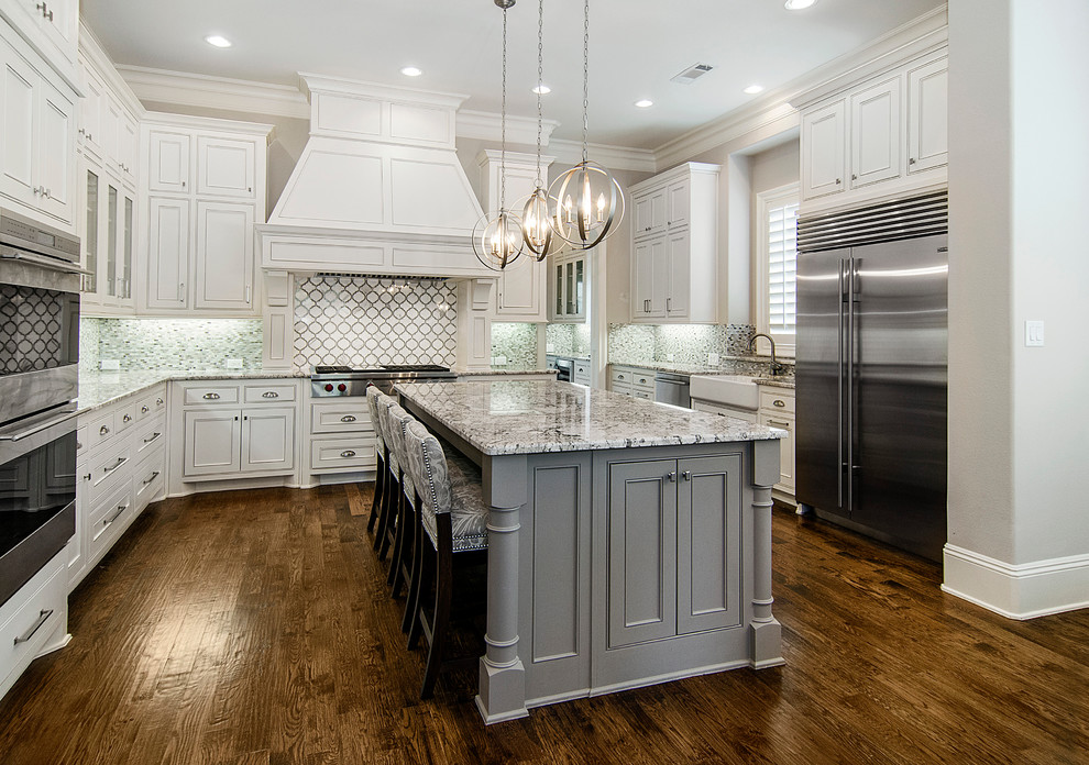 Klassische Küche in grau-weiß mit Landhausspüle, weißen Schränken, bunter Rückwand, Küchengeräten aus Edelstahl, dunklem Holzboden, Kücheninsel und Kassettenfronten in Dallas