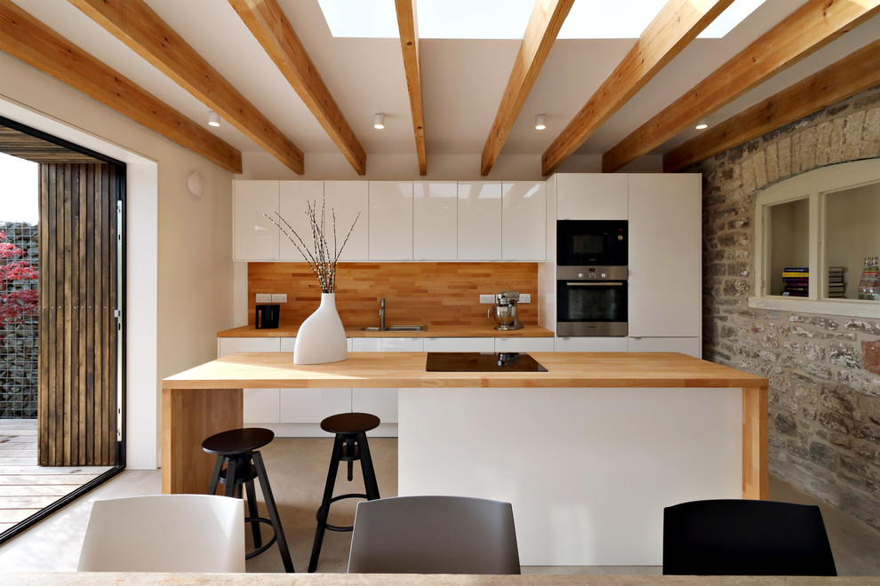 На фото: параллельная кухня-гостиная среднего размера в современном стиле с двойной мойкой, плоскими фасадами, белыми фасадами, деревянной столешницей, техникой из нержавеющей стали, бетонным полом и полуостровом с
