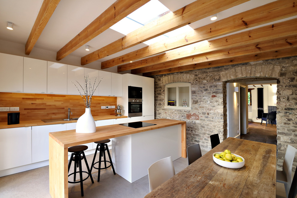 На фото: прямая кухня среднего размера в современном стиле с обеденным столом, двойной мойкой, плоскими фасадами, белыми фасадами, деревянной столешницей, техникой из нержавеющей стали, бетонным полом и полуостровом