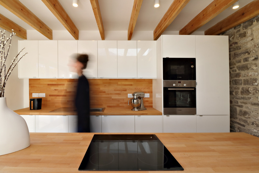 Photo of a small contemporary single-wall kitchen/diner in Other with a double-bowl sink, flat-panel cabinets, white cabinets, wood worktops, stainless steel appliances, concrete flooring and a breakfast bar.