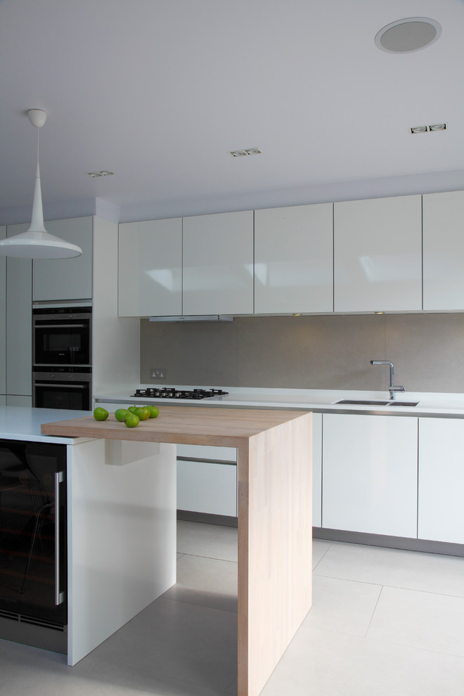 This is an example of a medium sized contemporary single-wall open plan kitchen in London with flat-panel cabinets, an island, an integrated sink, white cabinets, composite countertops, grey splashback, ceramic splashback, integrated appliances, ceramic flooring, grey floors, white worktops and a vaulted ceiling.