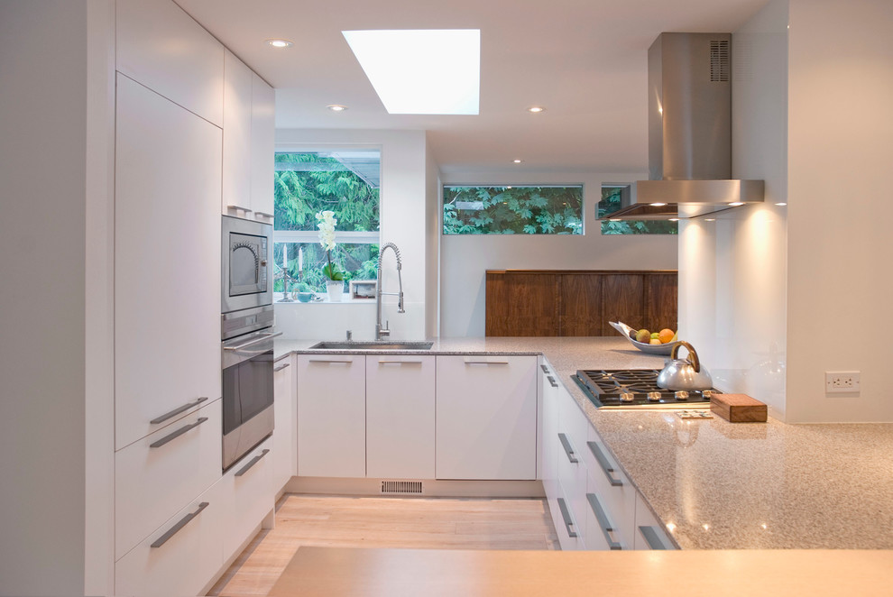 Contemporary u-shaped kitchen in Vancouver with a submerged sink, white cabinets, white splashback and integrated appliances.