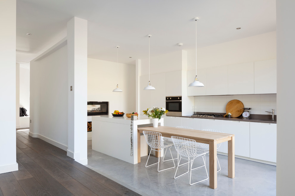 Example of a danish single-wall concrete floor eat-in kitchen design in London with flat-panel cabinets, white cabinets, an island, solid surface countertops and ceramic backsplash