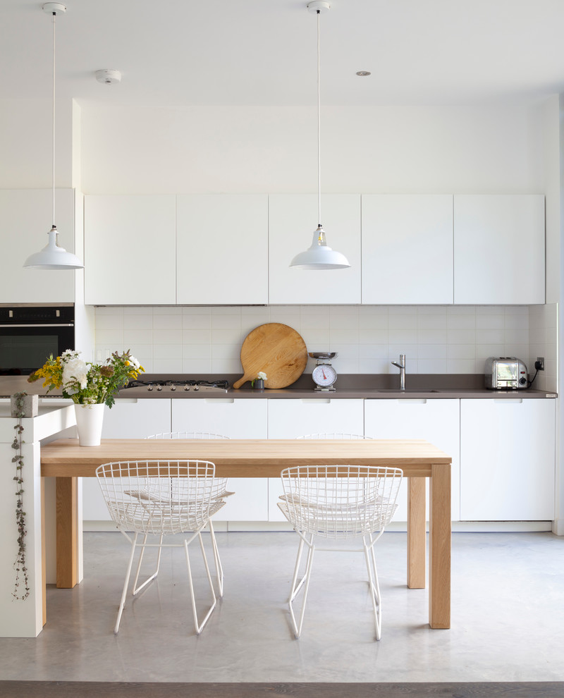 Nordische Küche mit flächenbündigen Schrankfronten, weißen Schränken, Küchenrückwand in Weiß und Kücheninsel in London