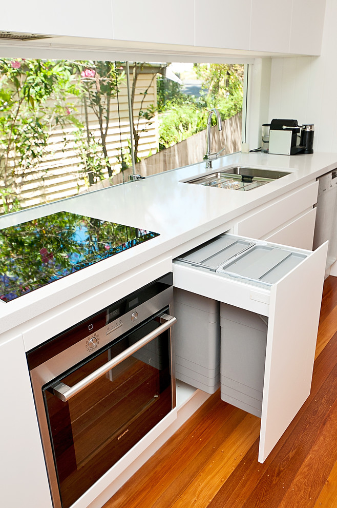 This is an example of a large modern galley open plan kitchen in Brisbane with a submerged sink, flat-panel cabinets, white cabinets, engineered stone countertops, stainless steel appliances, light hardwood flooring and an island.