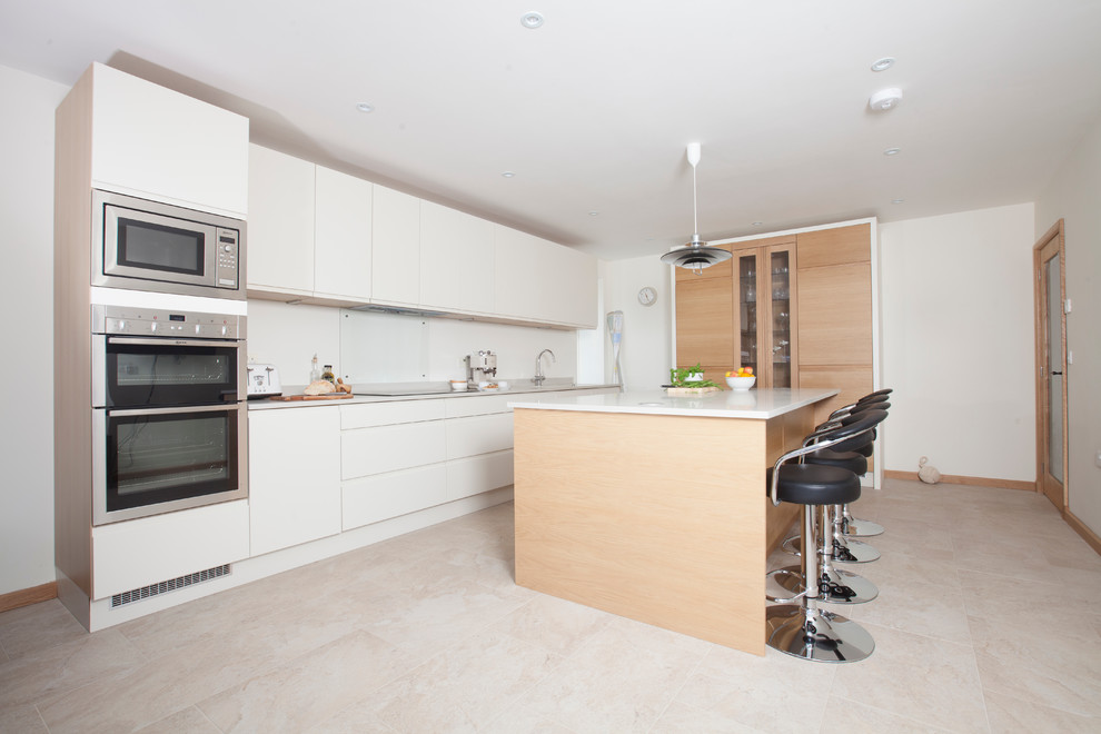 Inspiration for a medium sized contemporary l-shaped kitchen/diner in Cardiff with a built-in sink, flat-panel cabinets, white cabinets, composite countertops, glass tiled splashback, stainless steel appliances, ceramic flooring and an island.