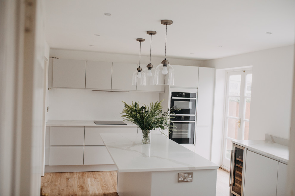 Bild på ett mellanstort funkis vit vitt kök och matrum, med en undermonterad diskho, släta luckor, grå skåp, bänkskiva i kvartsit, vitt stänkskydd, svarta vitvaror, laminatgolv, en köksö och brunt golv