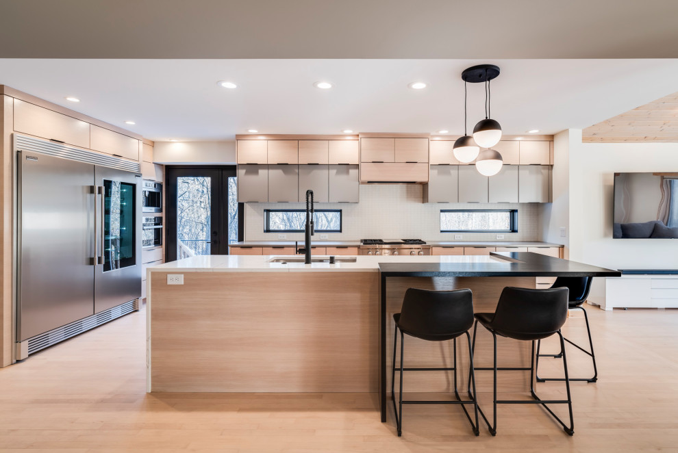This is an example of a modern l-shaped kitchen in Minneapolis with a submerged sink, flat-panel cabinets, light wood cabinets, stainless steel appliances, light hardwood flooring, an island, beige floors and grey worktops.