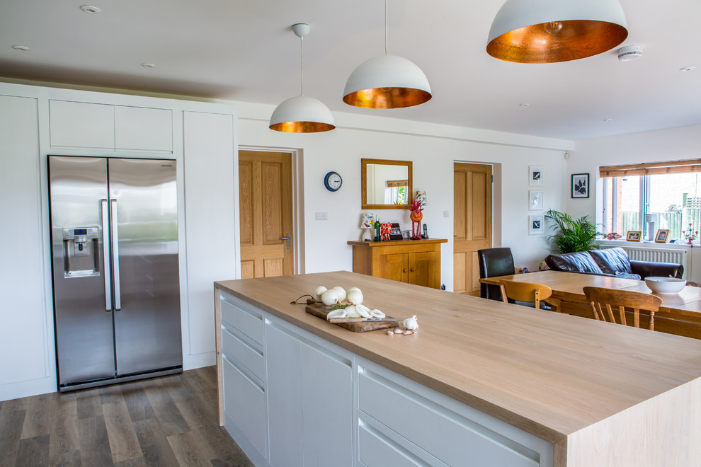 This is an example of a large contemporary u-shaped open plan kitchen in Other with a double-bowl sink, flat-panel cabinets, white cabinets, wood worktops, white splashback, porcelain splashback, light hardwood flooring and an island.