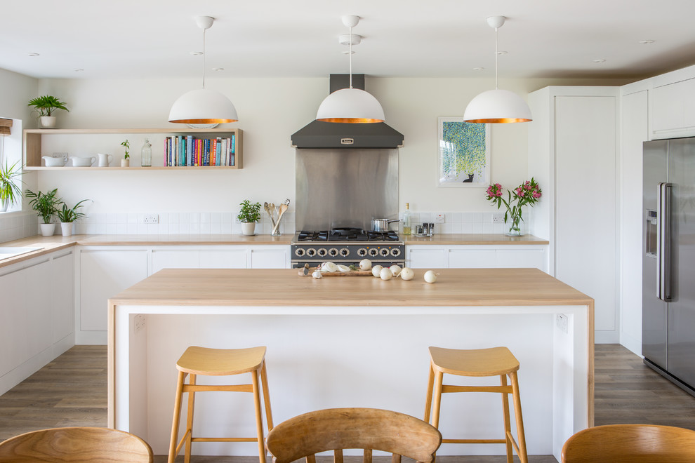 Large contemporary u-shaped open plan kitchen in Other with a double-bowl sink, flat-panel cabinets, white cabinets, wood worktops, white splashback, porcelain splashback, light hardwood flooring and an island.