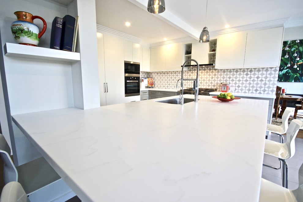 Bild på ett stort funkis vit vitt kök, med en undermonterad diskho, skåp i shakerstil, grå skåp, bänkskiva i kvarts, grått stänkskydd, stänkskydd i keramik, rostfria vitvaror, klinkergolv i porslin, en köksö och beiget golv
