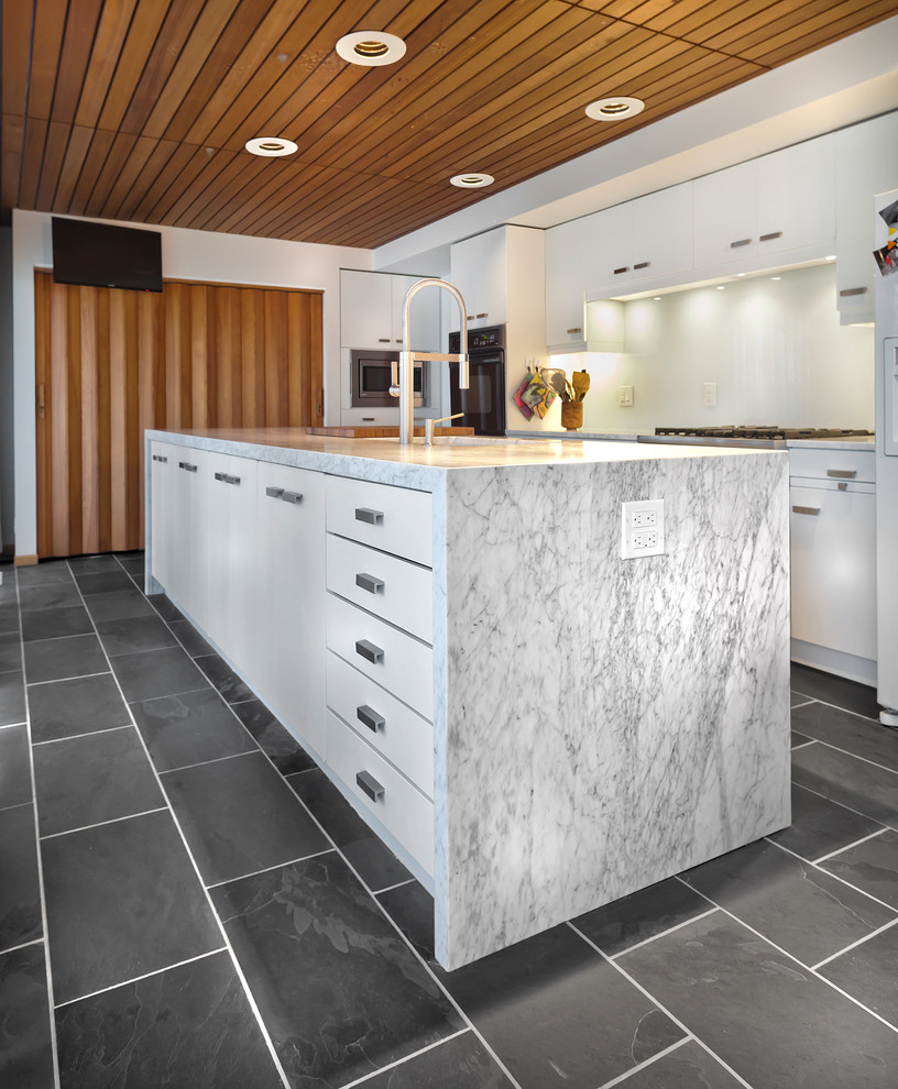 Design ideas for a medium sized contemporary single-wall kitchen/diner in Minneapolis with a submerged sink, flat-panel cabinets, white cabinets, marble worktops, white splashback, glass sheet splashback, stainless steel appliances, slate flooring and an island.