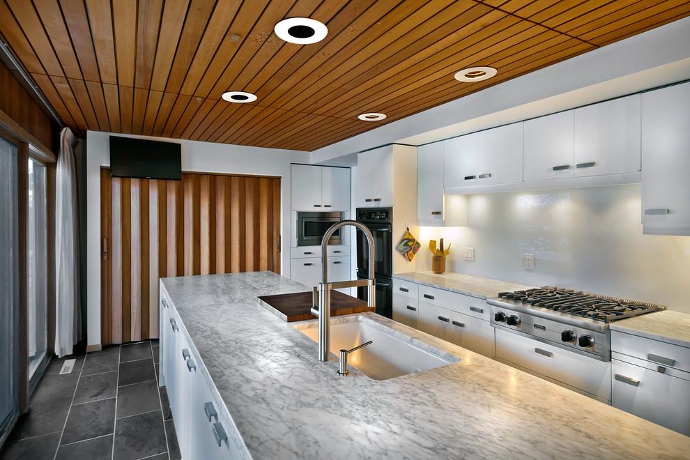 Example of a mid-sized trendy single-wall slate floor eat-in kitchen design in Minneapolis with an undermount sink, flat-panel cabinets, white cabinets, marble countertops, white backsplash, glass sheet backsplash, stainless steel appliances and an island