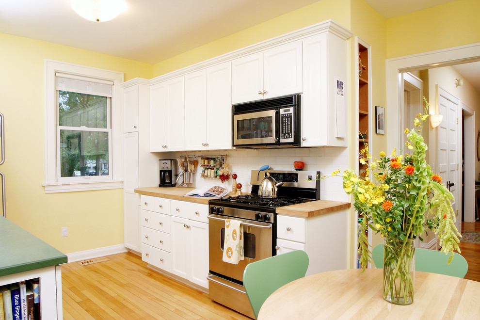 Small elegant galley light wood floor enclosed kitchen photo in Minneapolis with flat-panel cabinets, white cabinets, wood countertops, white backsplash, ceramic backsplash, stainless steel appliances and no island