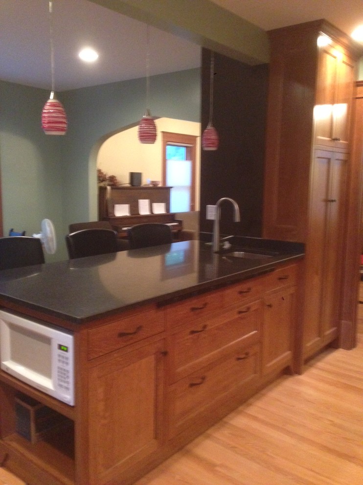 Inredning av ett amerikanskt mellanstort kök, med en undermonterad diskho, skåp i shakerstil, skåp i mellenmörkt trä, granitbänkskiva, svart stänkskydd, vita vitvaror, ljust trägolv och en halv köksö