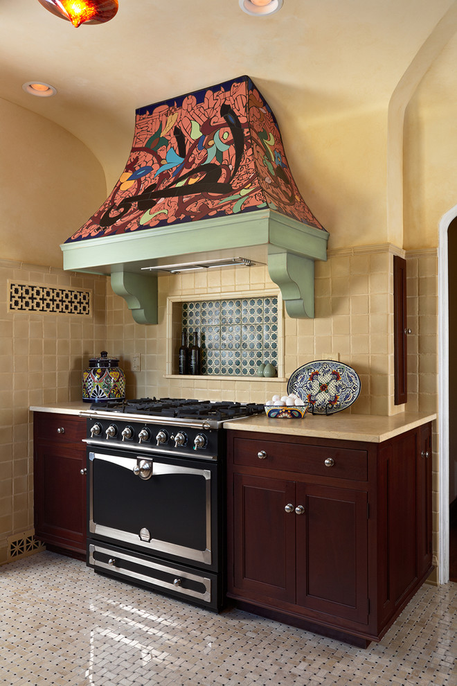 ミネアポリスにある高級な地中海スタイルのおしゃれなキッチン (シェーカースタイル扉のキャビネット、濃色木目調キャビネット、ベージュキッチンパネル、黒い調理設備) の写真