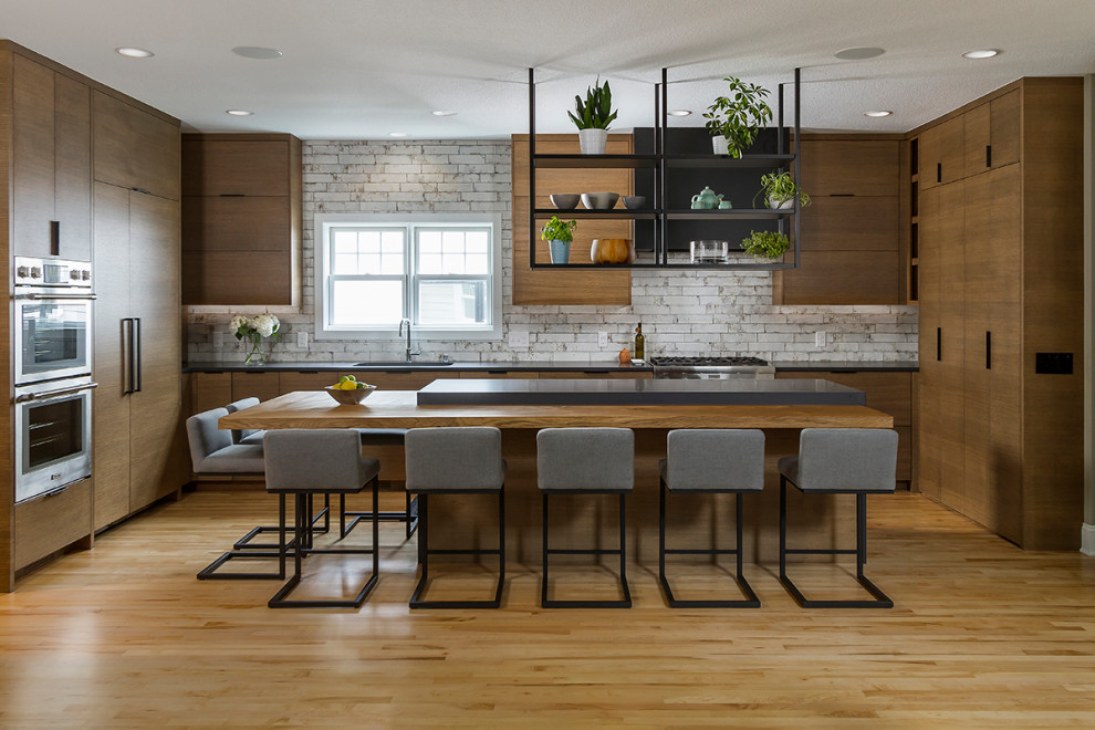 Inspiration for a modern u-shaped kitchen in Minneapolis with a submerged sink, flat-panel cabinets, brown cabinets, composite countertops, white splashback, light hardwood flooring, an island, black worktops and integrated appliances.