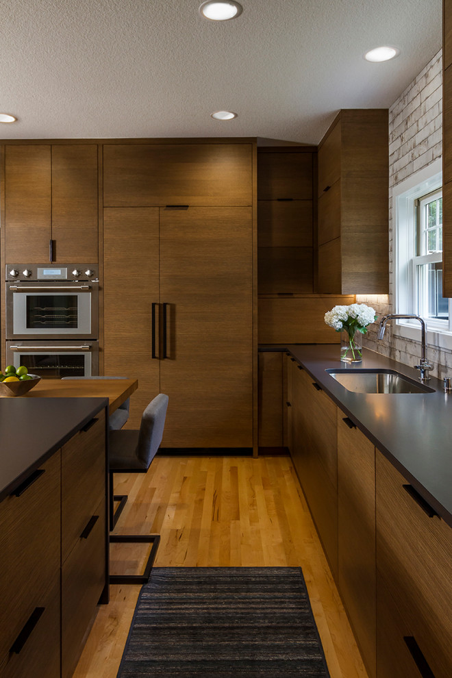 Eat-in kitchen - modern light wood floor eat-in kitchen idea in Minneapolis with an undermount sink, flat-panel cabinets, brown cabinets, solid surface countertops, white backsplash, ceramic backsplash, stainless steel appliances, an island and black countertops