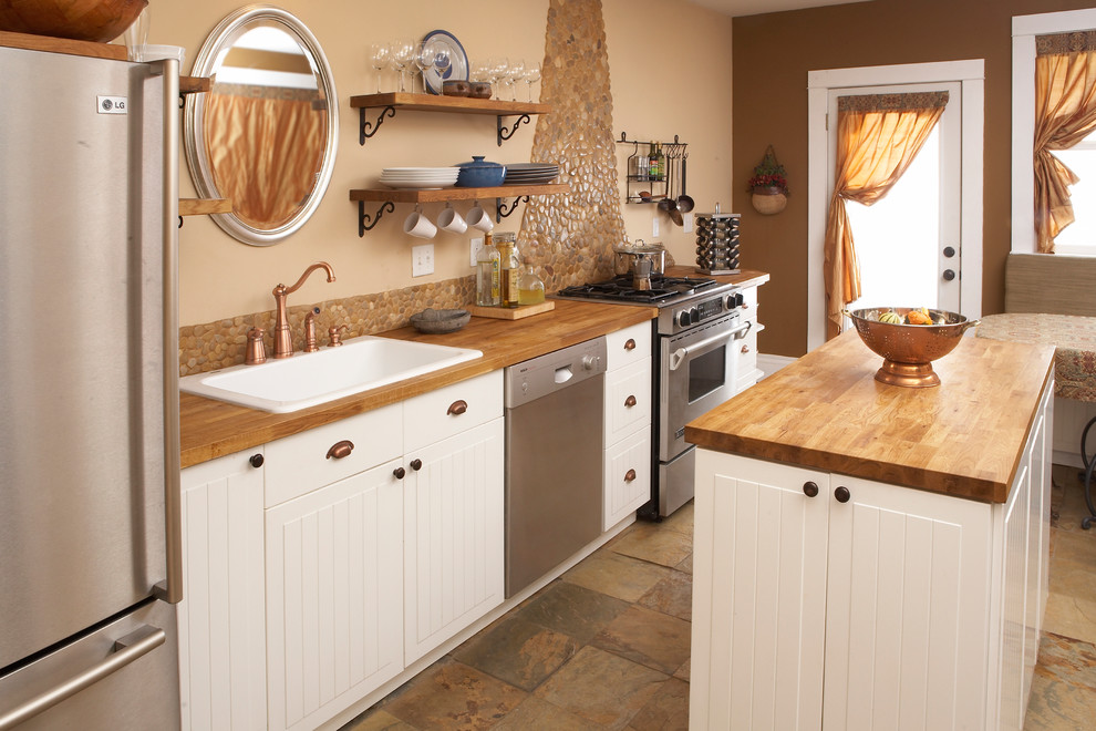 Modelo de cocina tradicional con electrodomésticos de acero inoxidable, encimera de madera, puertas de armario blancas, salpicadero marrón, salpicadero de azulejos de piedra y fregadero encastrado