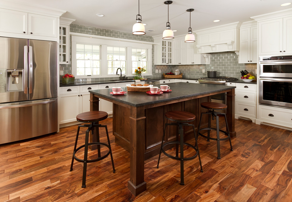 Inspiration for a large timeless l-shaped medium tone wood floor kitchen remodel in Minneapolis with an undermount sink, shaker cabinets, white cabinets, granite countertops, gray backsplash, subway tile backsplash, stainless steel appliances and an island