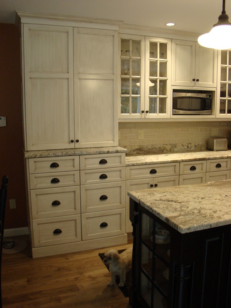 This is an example of a large classic l-shaped kitchen/diner in Portland Maine with recessed-panel cabinets, distressed cabinets, granite worktops, multi-coloured splashback, porcelain splashback, stainless steel appliances, light hardwood flooring and an island.