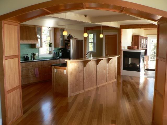 Bild på ett mellanstort amerikanskt kök, med skåp i ljust trä, grönt stänkskydd, stänkskydd i glaskakel, rostfria vitvaror, mellanmörkt trägolv och en köksö