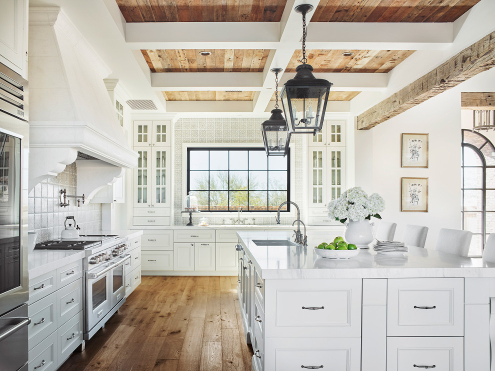 Exempel på ett klassiskt vit vitt kök, med en undermonterad diskho, luckor med infälld panel, vita skåp, grått stänkskydd, rostfria vitvaror, mellanmörkt trägolv, en köksö och brunt golv