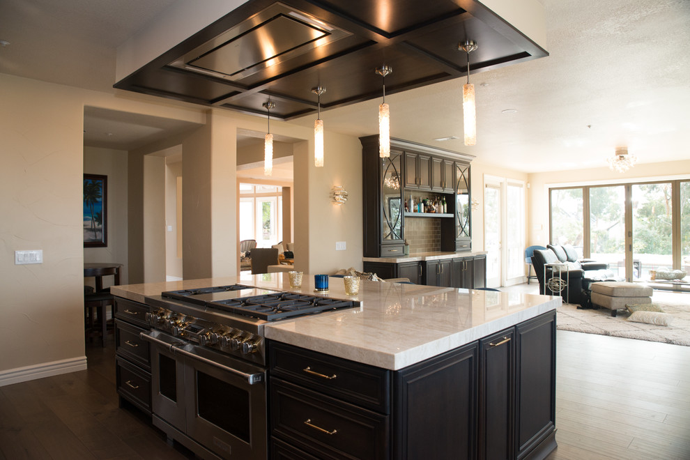 This is an example of a medium sized classic l-shaped open plan kitchen in San Diego with a submerged sink, recessed-panel cabinets, dark wood cabinets, quartz worktops, metallic splashback, glass tiled splashback, integrated appliances, medium hardwood flooring, an island, brown floors and white worktops.