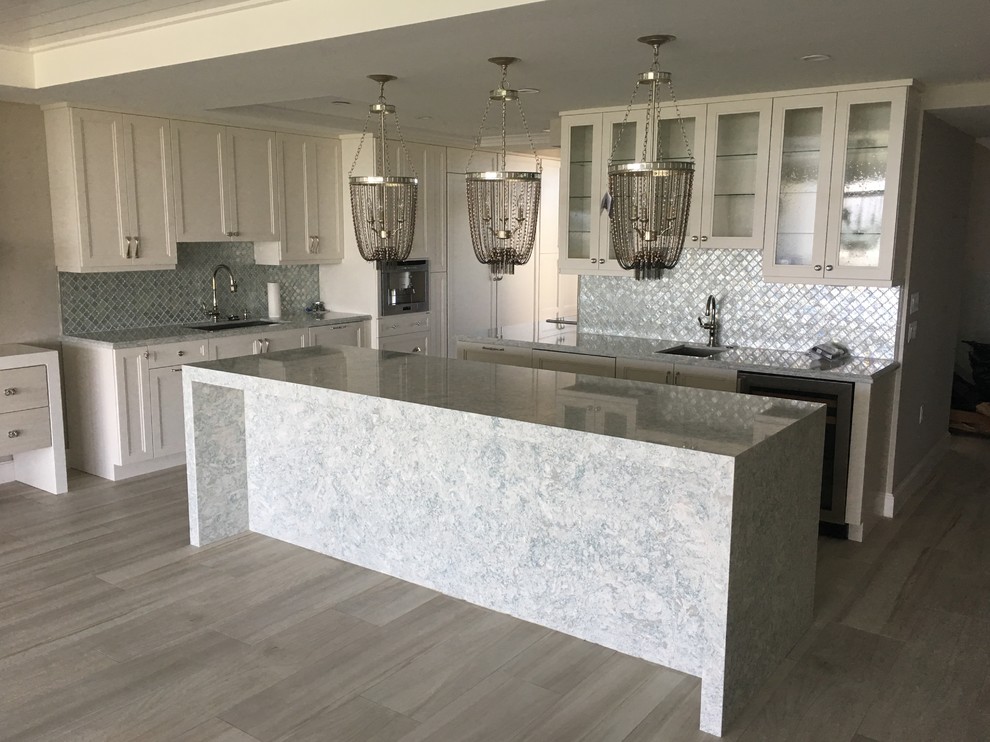 Design ideas for a large traditional l-shaped kitchen in Miami with a submerged sink, shaker cabinets, white cabinets, quartz worktops, grey splashback, glass tiled splashback, stainless steel appliances, light hardwood flooring, an island and beige floors.