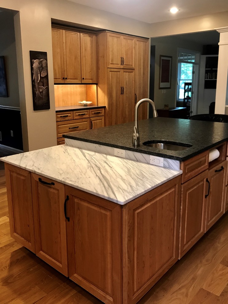 Klassisk inredning av ett stort grå grått kök och matrum, med en undermonterad diskho, luckor med upphöjd panel, skåp i mellenmörkt trä, granitbänkskiva, beige stänkskydd, stänkskydd i cementkakel, rostfria vitvaror, mellanmörkt trägolv, en köksö och gult golv
