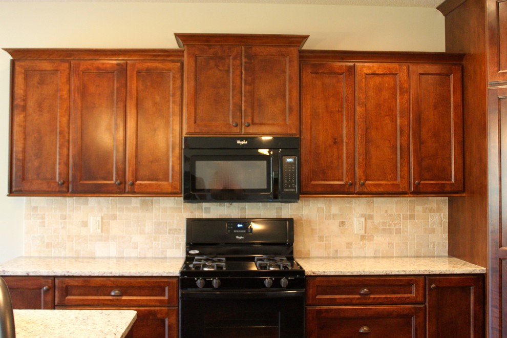 Immagine di una cucina classica con ante lisce, ante in legno scuro, top in granito, paraspruzzi beige, paraspruzzi con piastrelle in pietra e elettrodomestici neri