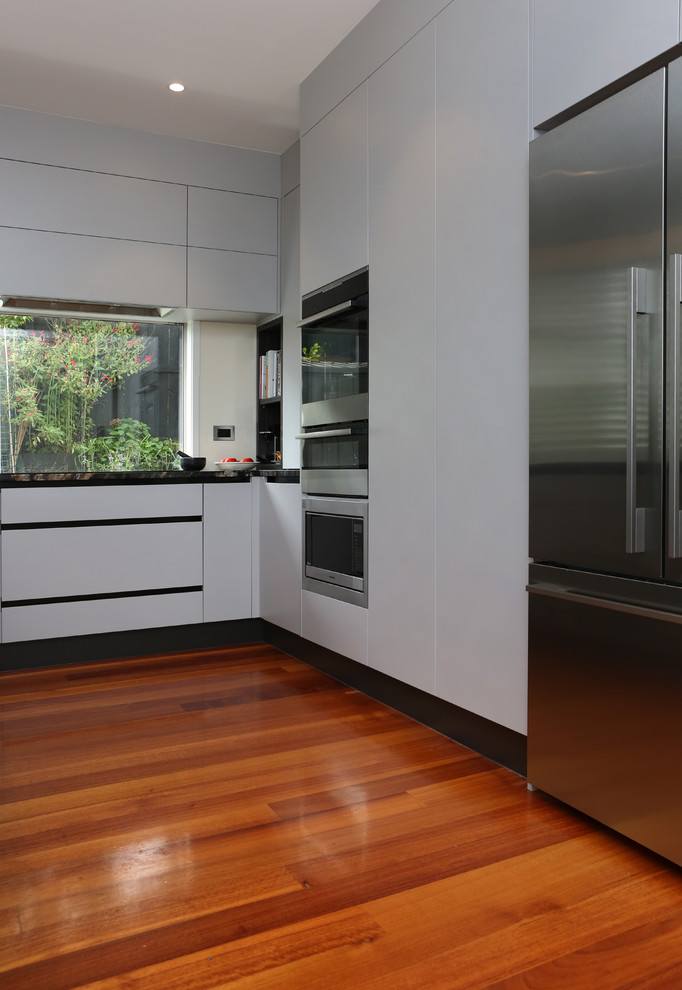 Inspiration for a large contemporary u-shaped open plan kitchen in Auckland with a submerged sink, flat-panel cabinets, grey cabinets, granite worktops, stainless steel appliances, medium hardwood flooring, an island and multi-coloured floors.