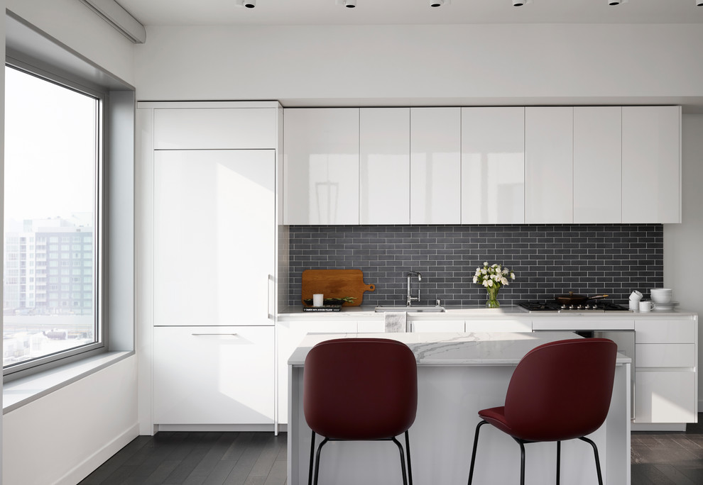 Foto på ett litet funkis vit linjärt kök med öppen planlösning, med en enkel diskho, släta luckor, svart stänkskydd, stänkskydd i tunnelbanekakel, mörkt trägolv, en köksö, brunt golv, integrerade vitvaror och bänkskiva i kvarts
