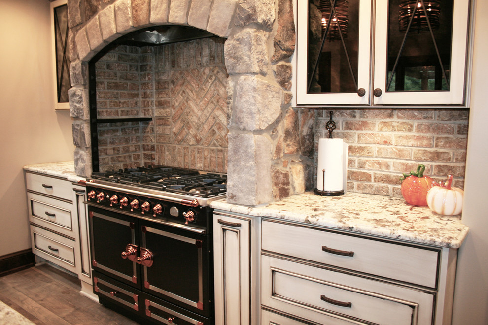 Inredning av ett medelhavsstil stort kök, med luckor med profilerade fronter, vita skåp, granitbänkskiva, brunt stänkskydd, stänkskydd i tegel, svarta vitvaror, mellanmörkt trägolv och brunt golv