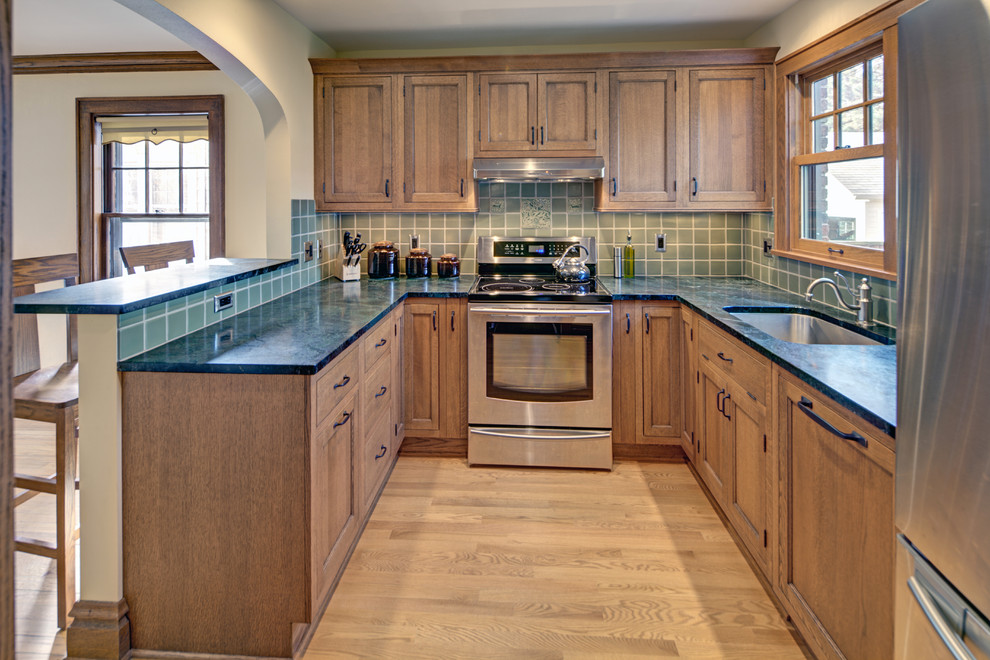 Foto på ett litet amerikanskt kök, med en undermonterad diskho, luckor med profilerade fronter, skåp i mellenmörkt trä, bänkskiva i täljsten, grönt stänkskydd, stänkskydd i keramik, rostfria vitvaror, mellanmörkt trägolv och flera köksöar