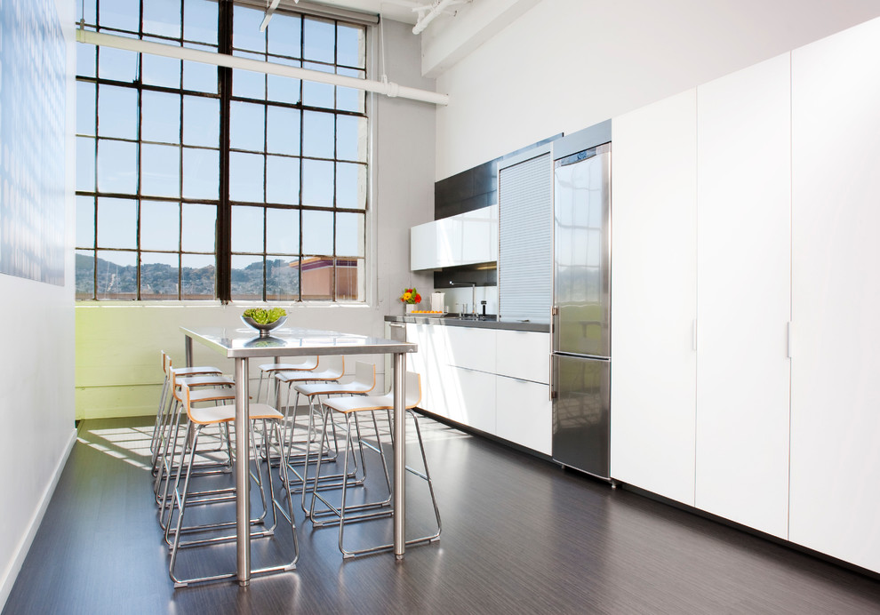 Bild på ett litet funkis linjärt kök och matrum, med en undermonterad diskho, släta luckor, vita skåp, bänkskiva i koppar, vitt stänkskydd, rostfria vitvaror, laminatgolv och brunt golv