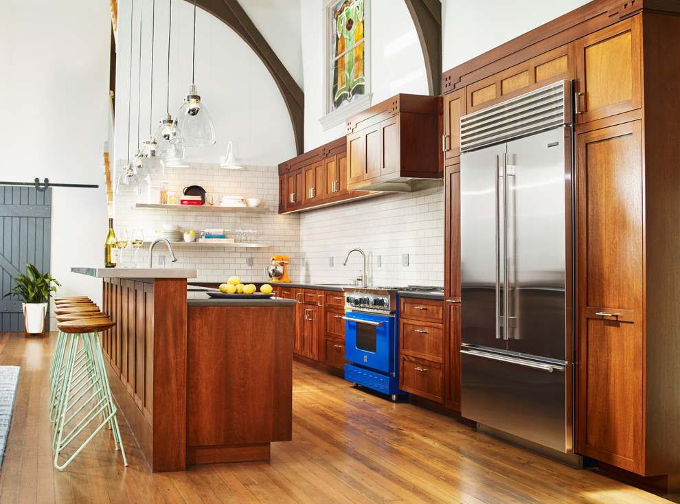 Bild på ett mellanstort eklektiskt l-kök, med brunt golv, skåp i shakerstil, skåp i mellenmörkt trä, vitt stänkskydd, stänkskydd i tunnelbanekakel, rostfria vitvaror, mellanmörkt trägolv och en köksö