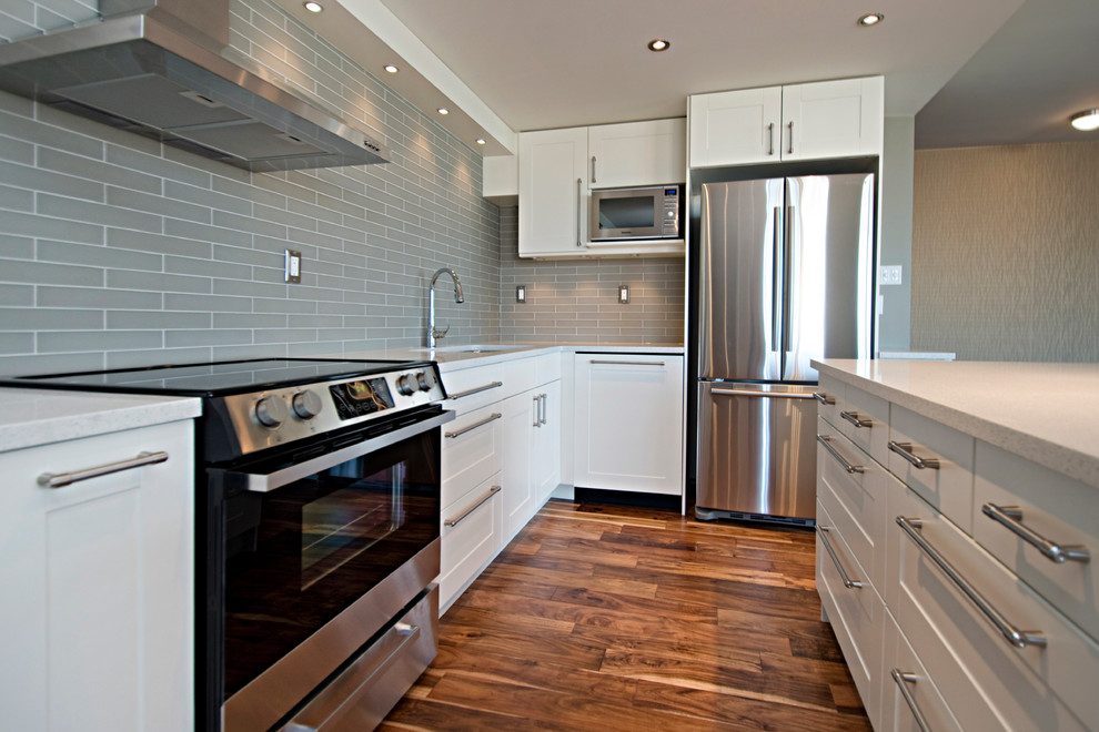 Small transitional l-shaped medium tone wood floor open concept kitchen photo in Calgary with an undermount sink, shaker cabinets, white cabinets, quartz countertops, multicolored backsplash, glass tile backsplash, stainless steel appliances and an island